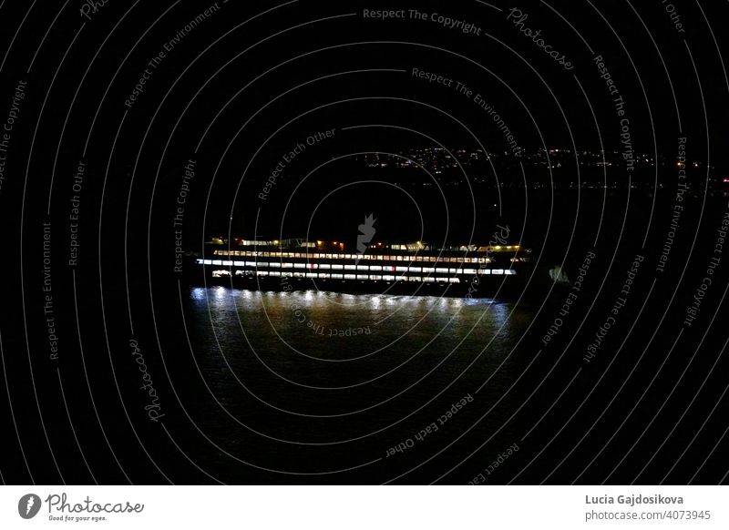 The Seattle–Bainbridge ferry lighted by cabin and navigational lights is passing during the night between Seattle and Bainbridge Island, Washington across Puget Sound. In the background are lights of Seattle suburbs with a lot of copy space.