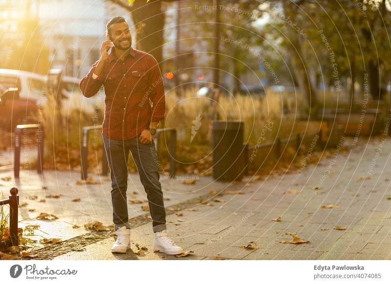 Handsome young man using mobile phone at the street Sinhalese asian Indian bearded outside urban standing outdoors city Warsaw casual lifestyle guy attractive