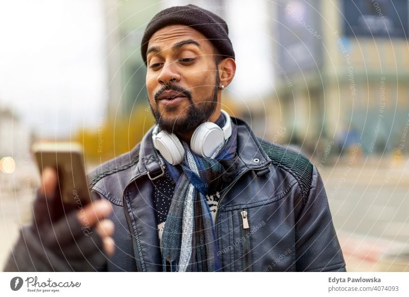 Handsome young man using mobile phone at the street Sinhalese asian Indian bearded outside urban standing outdoors city Warsaw casual lifestyle guy attractive