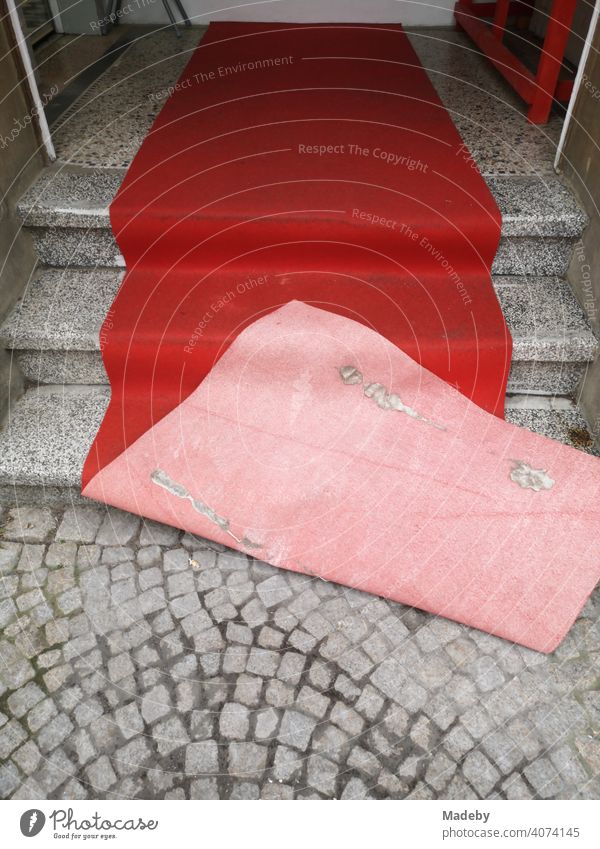 Red blown carpet on old grey steps and grey cobblestone pavement at the entrance of a hairdresser in the old town of Oerlinghausen near Bielefeld at the Hermannsweg in the Teutoburg Forest in East Westphalia-Lippe