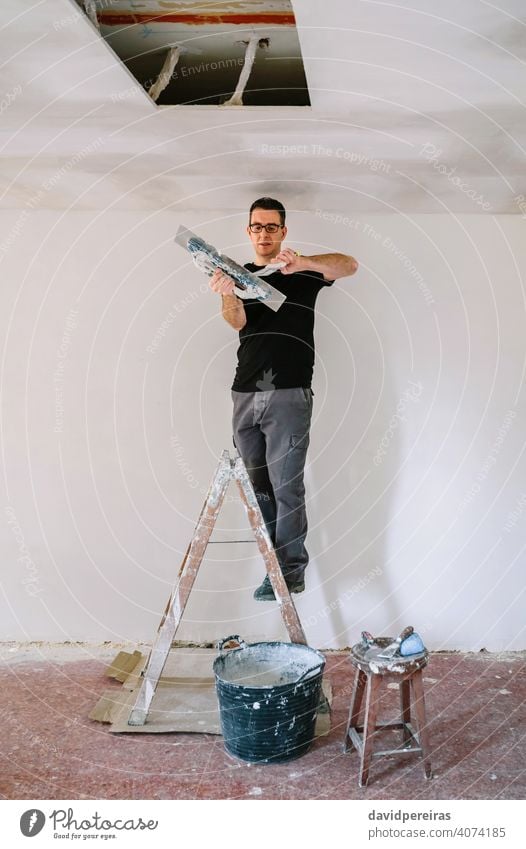 Builder working picking plaster with spatula mason builder plasterer picking up gypsum plaster trowel climbed on ladder home improvement reform house stepladder