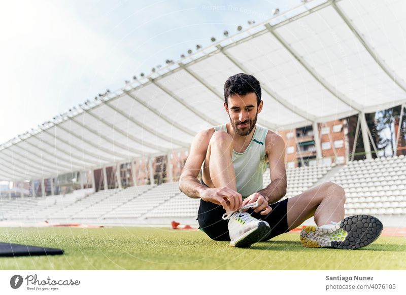 Male Athlete Tying Shoelace on Sports Track athlete sports track sitting 30s shoelace caucasian ethnicity tying athleticism sunlight dedication determination