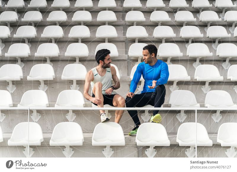 Front View of Friends Athletes talking athletes two people friends smiling sports track using phone sitting diversity black man rest resting bleachers smile