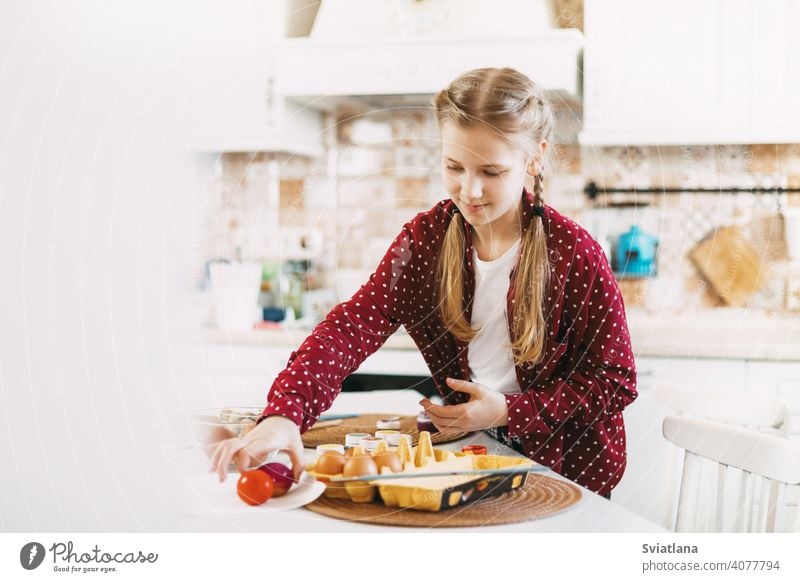 Little blonde at home in the kitchen paints Easter eggs in different colors for Easter easter spring child holiday preparation sisters brother bright family