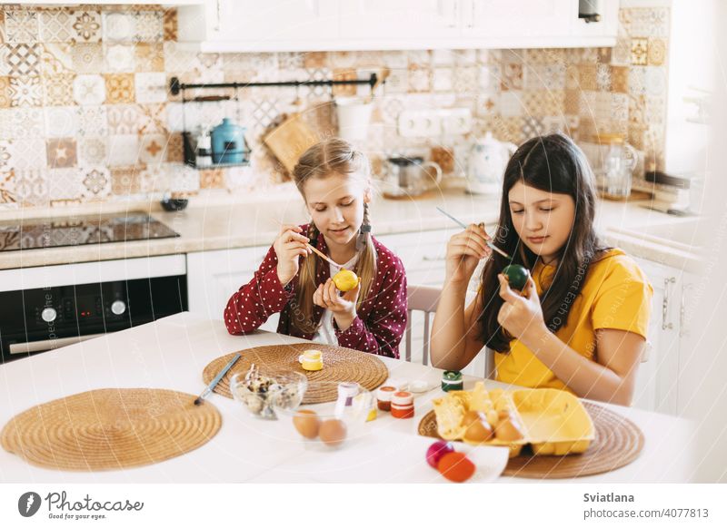 Two sisters are sitting at the table and painting Easter eggs in different colors for Easter easter spring child holiday preparation bright family girl white