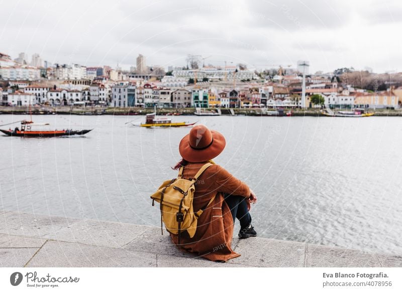 back view of young beautiful woman sitting by the river at sunset enjoying Porto views. Travel concept travel city sightseeing urban caucasian people