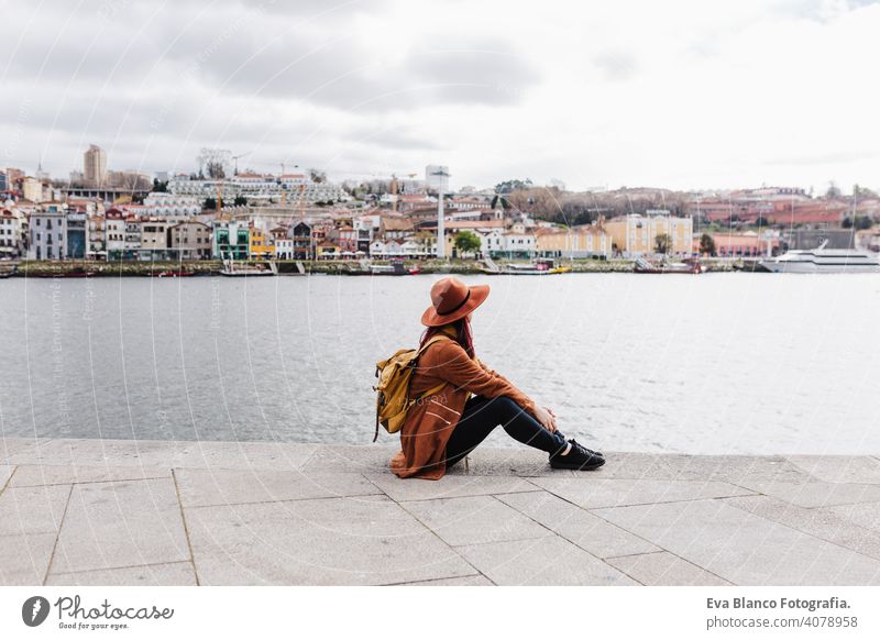 back view of young beautiful woman sitting by the river at sunset enjoying Porto views. Travel concept travel city sightseeing urban caucasian people