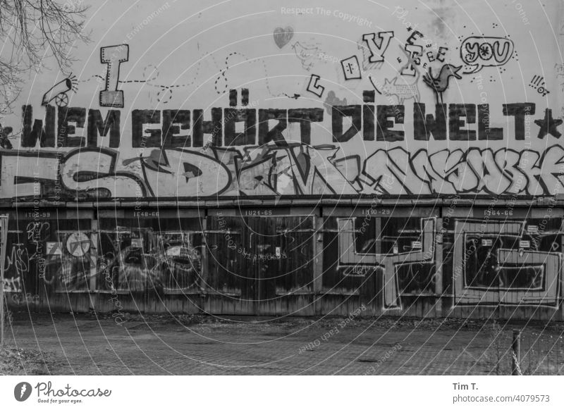 a graffiti on the facade above the garages "Who owns the world". Graffiti Lake Weißensee Berlin Garage door old Deserted Exterior shot Wall (building)