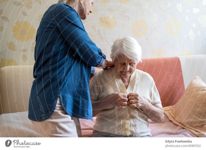 Woman helping senior woman dress in her bedroom getting dressed two people family mother daughter love together parent caregiver friendly assistance trust