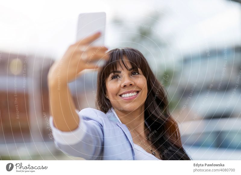 Attractive young woman using smartphone in the city hispanic latin smiling summer fun joy happy happiness urban girl people female lifestyle outdoors adult