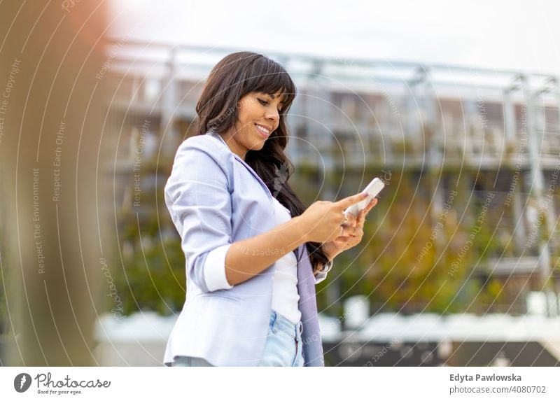 Attractive young woman using smartphone in the city hispanic latin smiling summer fun joy happy happiness urban girl people female lifestyle outdoors adult