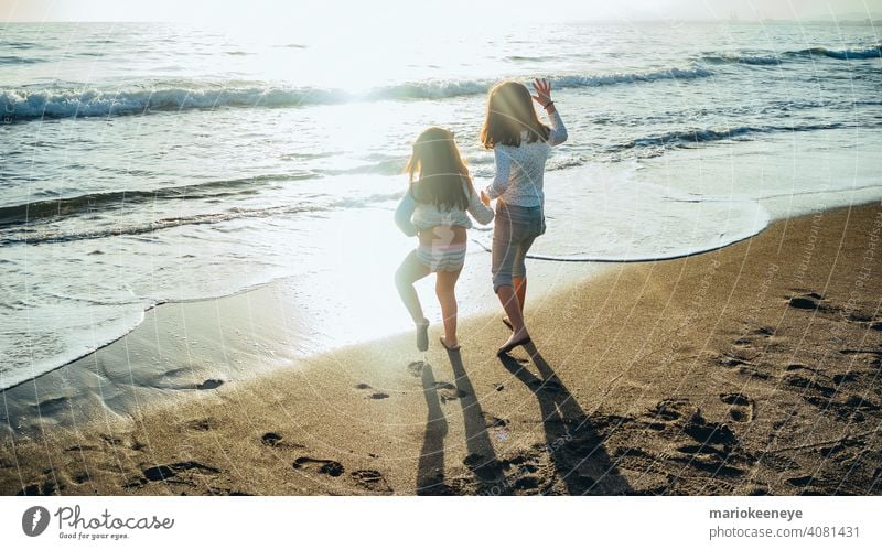 Back view of two little girls holding hands in front of the sea on a sunny afternoon. Concept of friendship two people horizontal togetherness females children