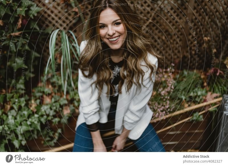 Smiling woman sitting on planter in garden plants smiling style backyard green flora female trendy cheerful excited joy happy lifestyle leisure organic natural