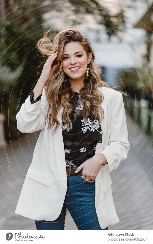 Charming lady touching hair on street woman city smiling young urban lifestyle leisure sensual female trendy windy toothy cheerful happy joy elegant town casual