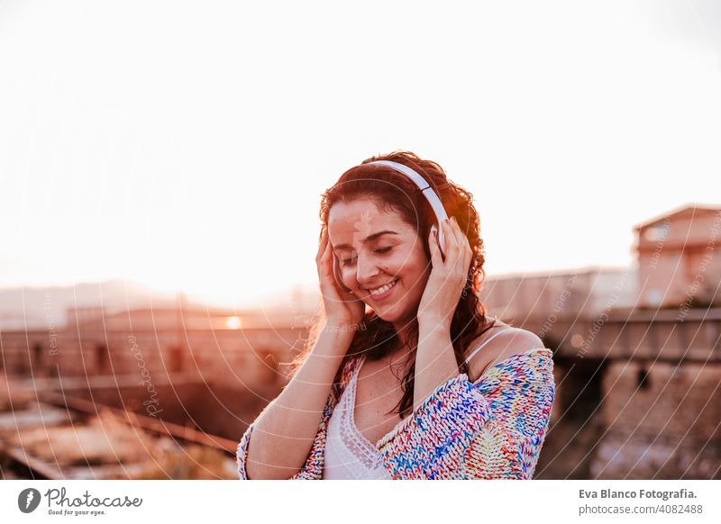 portrait outdoors of a young beautiful woman at sunset listening music on headset and smiling. Lifestyle and music concept casual fun young adult app