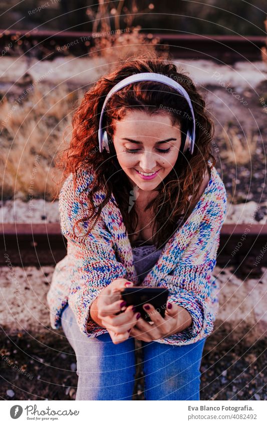 portrait outdoors of a young beautiful woman at sunset listening music on headset and smiling. Lifestyle and music concept casual fun young adult app