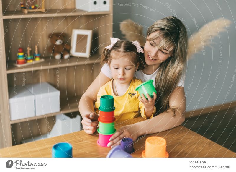 Mom and baby girl play with colorful molds and build a pyramid at the table at home. Time together, motherhood, child game preschool parent mom learning cute