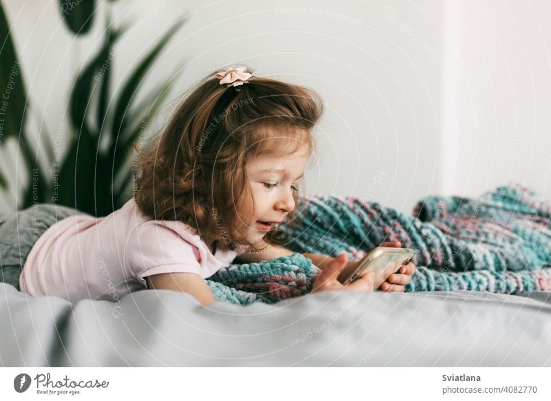 A little girl watches cartoons on her phone or plays on the bed before going to bed smartphone child kid mobile home small communication looking bedtime people