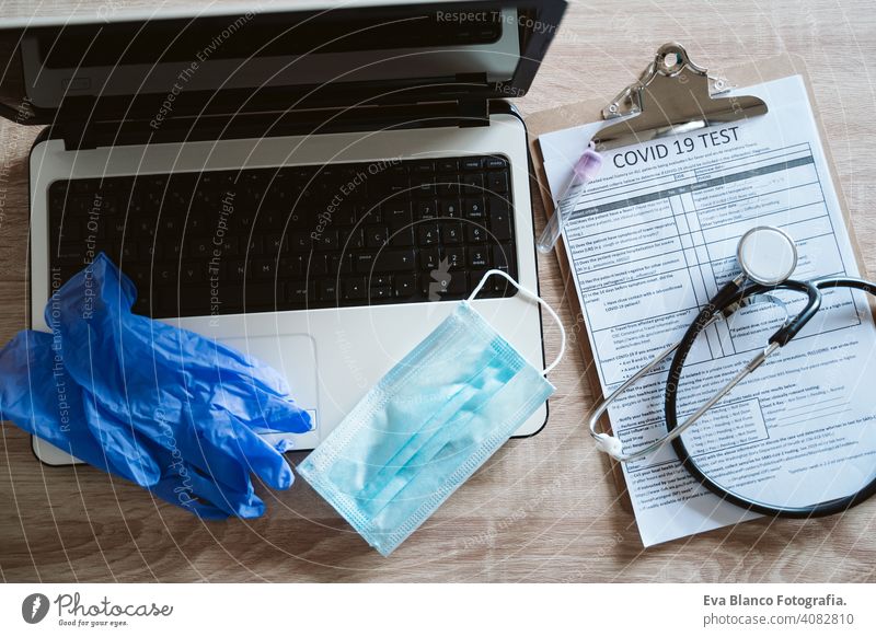 top view of a doctor workspace with laptop, protective gloves, protective mask, stethoscope and corona virus test. Covid-19 concept covid-19 nobody technology