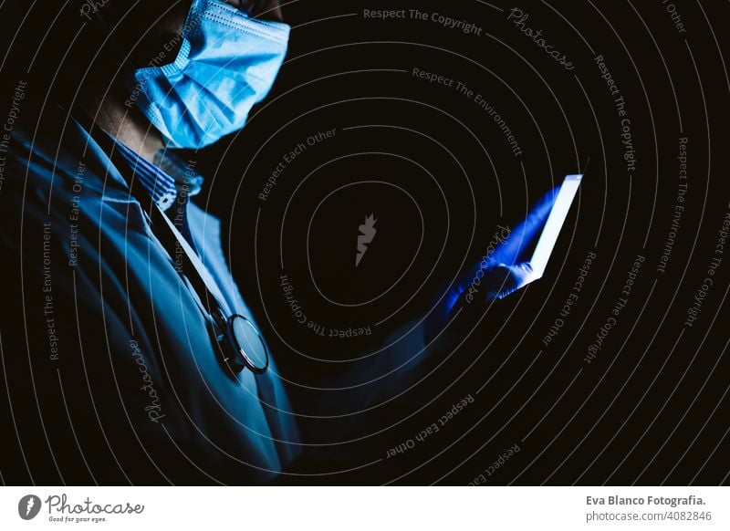 doctor man indoors, using mobile phone. Wearing protective gloves, mask and stethoscope. coronavirus covid-19 concept internet tecgnology dark corna virus