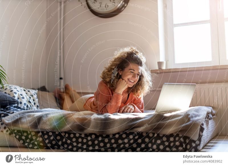 Young woman working in bed at home with laptop education learning studying homework book e-learning technology computer internet online communication wireless