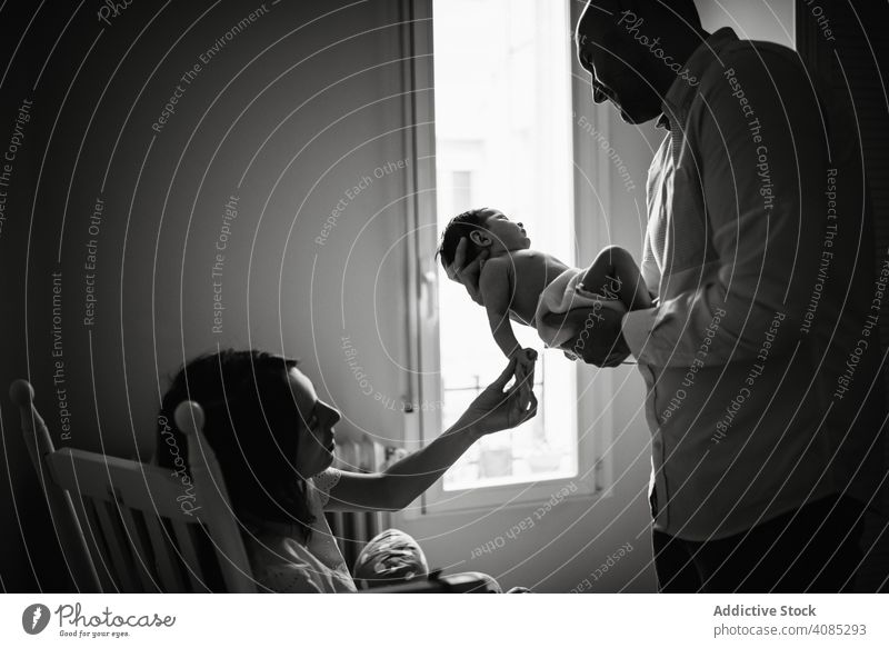 Parents holding baby in room parents touching care tender family love home bonding man woman mother father together joy newborn infant kid child speaking