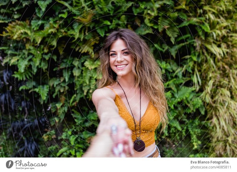 portrait of a young blonde beautiful woman at the street smiling. Holding hands in a follow me pose. Green vegetation background. Lifestyle outdoors. Summertime