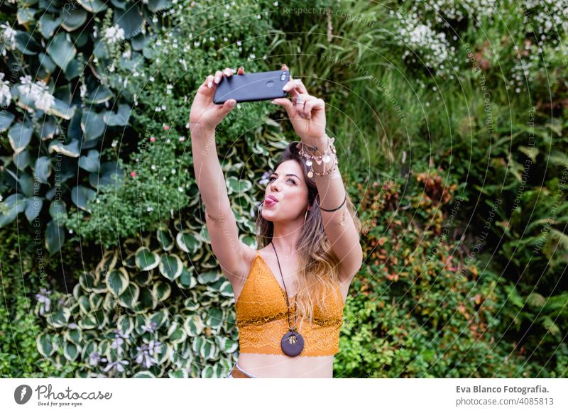 young blonde beautiful woman at the street taking a picture with mobile phone and smiling. Lifestyle outdoors. Summertime, Green background smart urban happy