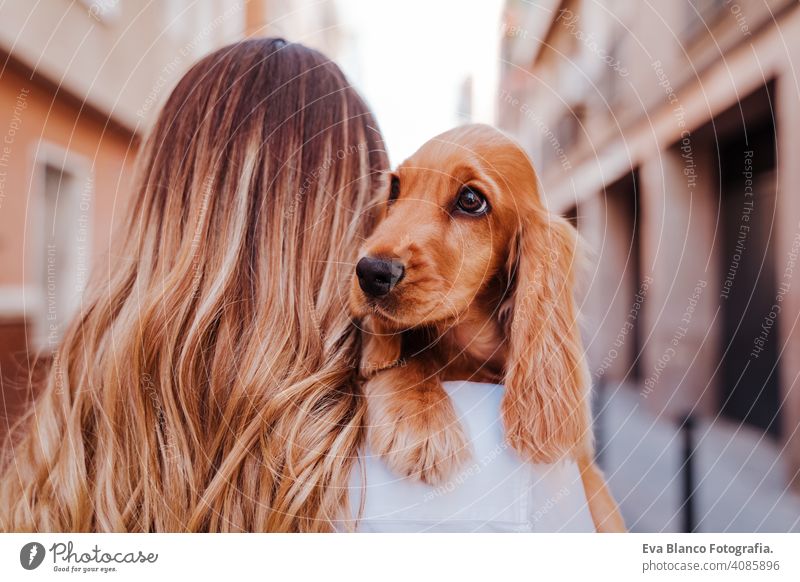 young woman at the street holding with her cute cocker dog on shoulder. Lifestyle outdoors with pets walking city urban purebred caucasian coker lifestyle