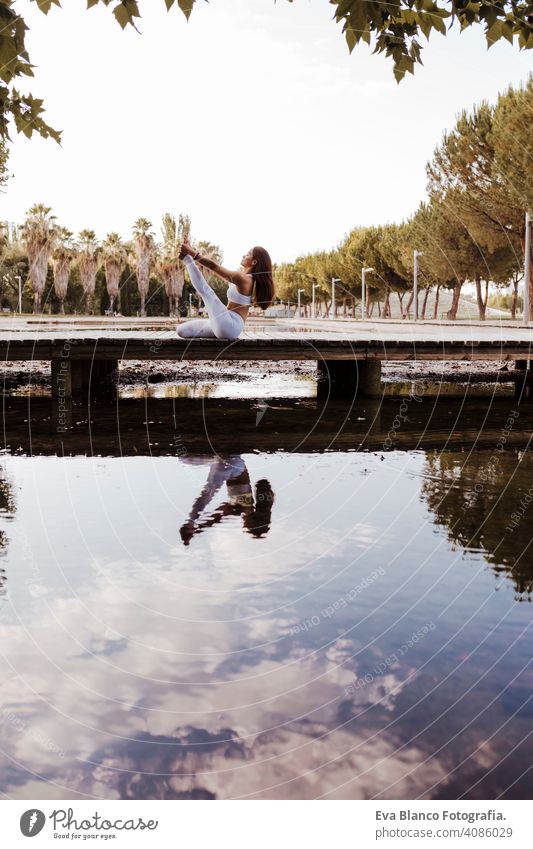 young beautiful asian woman doing yoga in a park. Sitting on the bridge with reflection on the water lake. Yoga and healthy lifestyle concept practicing balance