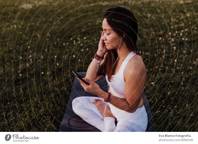 young beautiful asian woman relaxed after her yoga practice listening to music on earphones and mobile phone. Yoga and healthy life concept summer happy