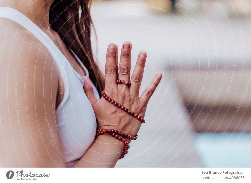 close up view of unrecognizable young asian woman doing yoga in a park. Sitting on the bridge with praying hands position and using Mala necklace. Yoga and healthy lifestyle concept