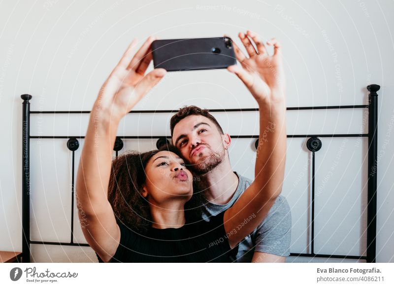 happy couple in love at home. Afro american woman and caucasian man taking a selfie with mobile phone. ethnic love concept afro american bed indoors valentine