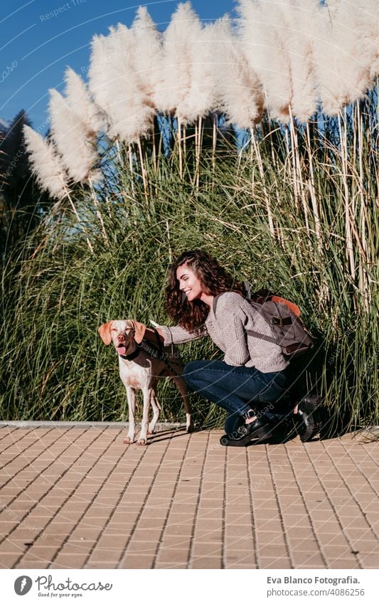 young woman and her dog outdoors in a park. sunny day, autumn season love pet owner beautiful happy smile mixed race purebred breed hug backpack walking