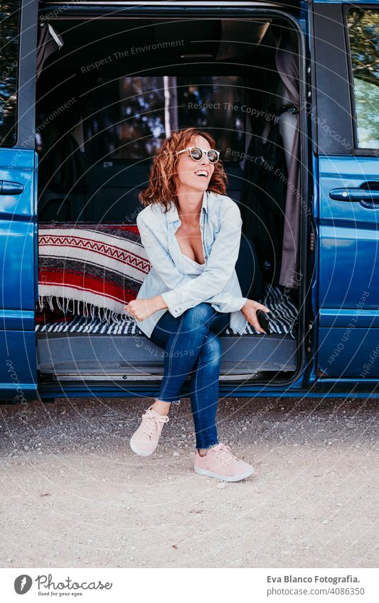 happy woman sitting in a blue van and having fun. travel concept. woman using mobile phone laugh car enjoying outdoors resting camp path way sunset wanderlust