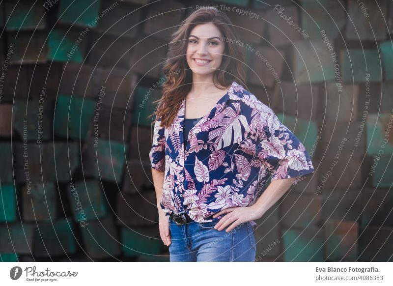 portrait of a young beautiful woman wearing casual clothes, standing over green wood blocks background and smiling. Outdoors lifestyle. nice youth student