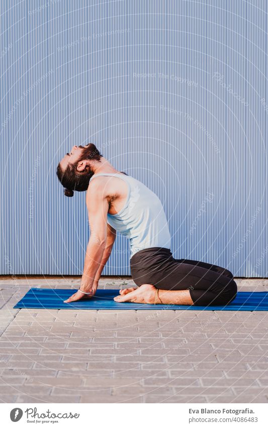 man in the city practicing yoga sport. blue background. healthy lifestyle outdoors muscular young handsome hispanic caucasian sportswear urban concentration