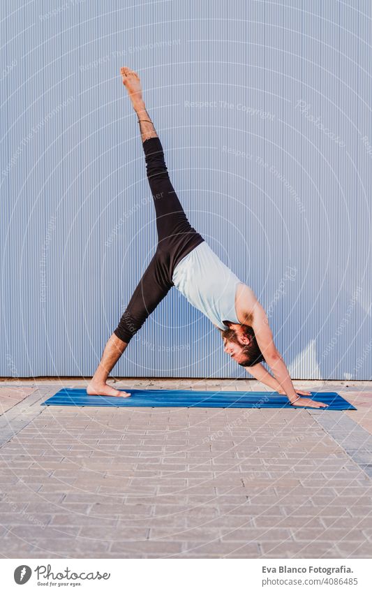 man in the city practicing yoga sport. blue background. healthy lifestyle outdoors muscular young handsome hispanic caucasian sportswear urban concentration