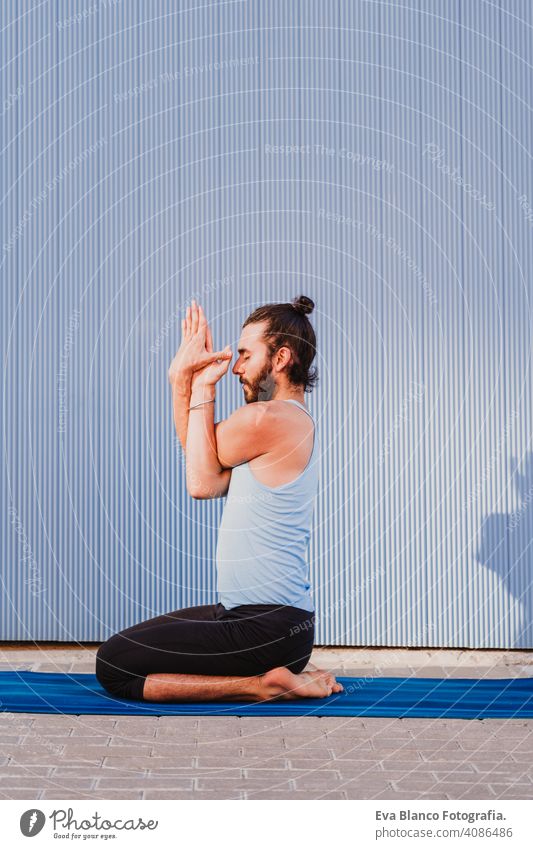 man in the city practicing yoga sport. blue background. healthy lifestyle outdoors muscular young handsome hispanic caucasian sportswear urban concentration