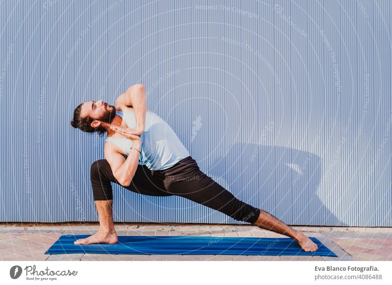 man in the city practicing yoga sport. blue background. healthy lifestyle outdoors muscular young handsome hispanic caucasian sportswear urban concentration