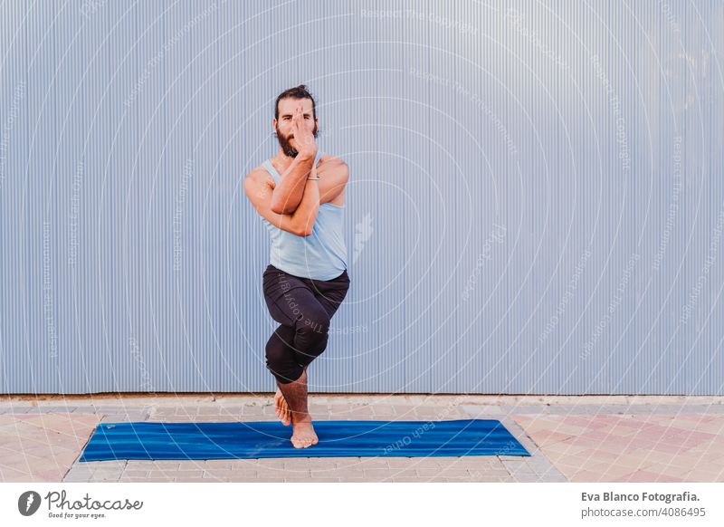 man in the city practicing yoga sport. blue background. healthy lifestyle outdoors muscular young handsome hispanic caucasian sportswear urban concentration