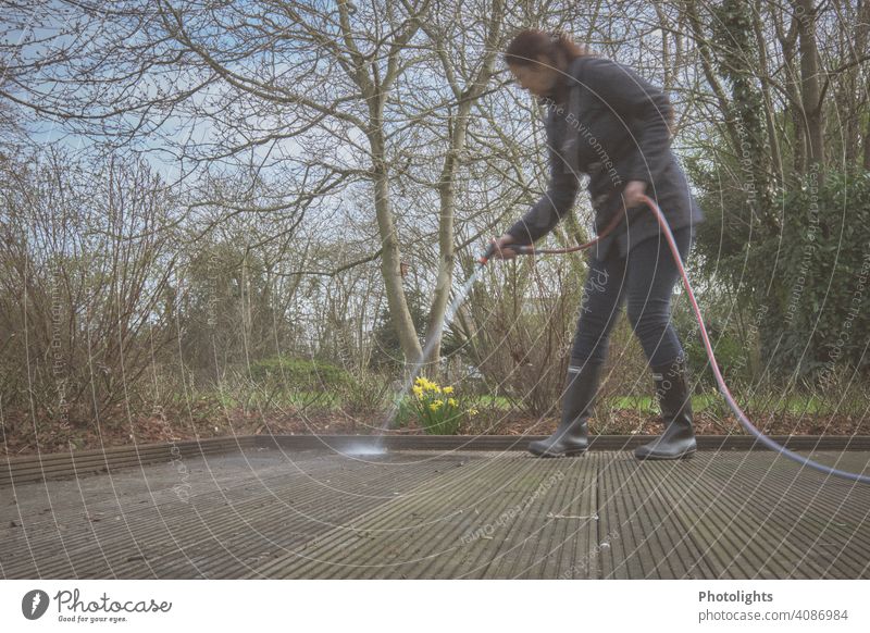 Woman cleans a wooden terrace with garden hose Cleaning Garden hose Water Jet of water Terrace Wet Drops of water Colour photo Exterior shot trees