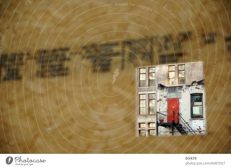 View through construction fence of dilapidated house with red door in Brooklyn, New York Fence Hoarding Vista Opening Hollow Peephole