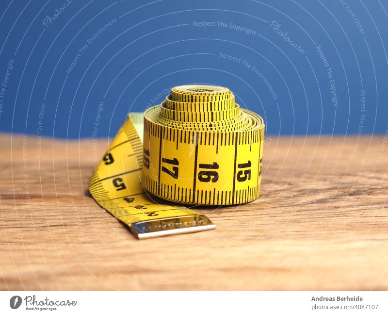 Yellow tailor tape measure on a wooden table, close up precision healthy overweight perfect centimeters professional ideal size concept skill diet designer