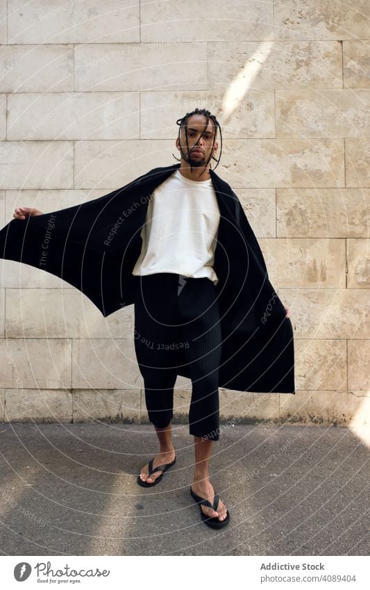 Trendy black guy posing on street man fashionable dynamic movement wall model hands in pockets african american city young stylish sunny daytime male lifestyle