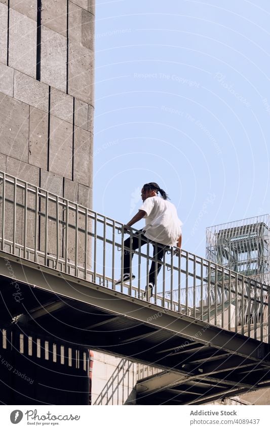 Black male sitting on bridge man city street equilibrium railing balance african american urban sunny daytime young casual lifestyle leisure rest relax modern