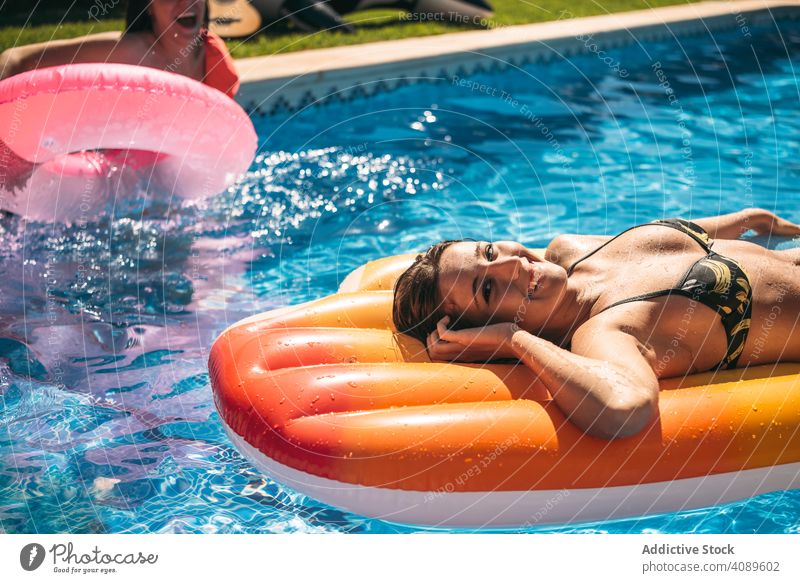 Young woman relaxing in pool with friends people resort having fun vacation summer holidays recreational swimming outdoors young leisure group floating