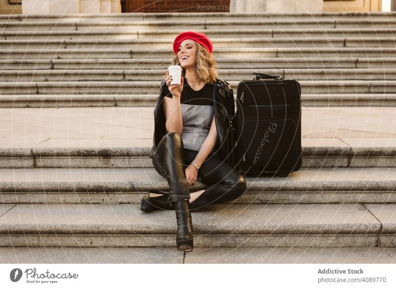 Cheerful tourist drinking on steps woman stairs suitcase smiling looking away joy takeaway stylish female young lifestyle leisure happy cheerful laughing