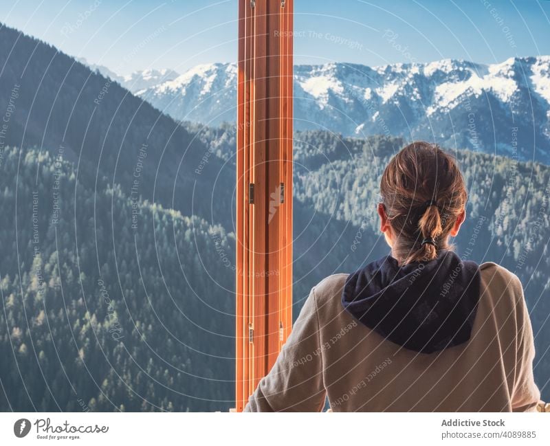 Anonymous woman looking at mountains from window admiring leaning sill home sunny daytime carefree female nature countryside lifestyle leisure rest relax view