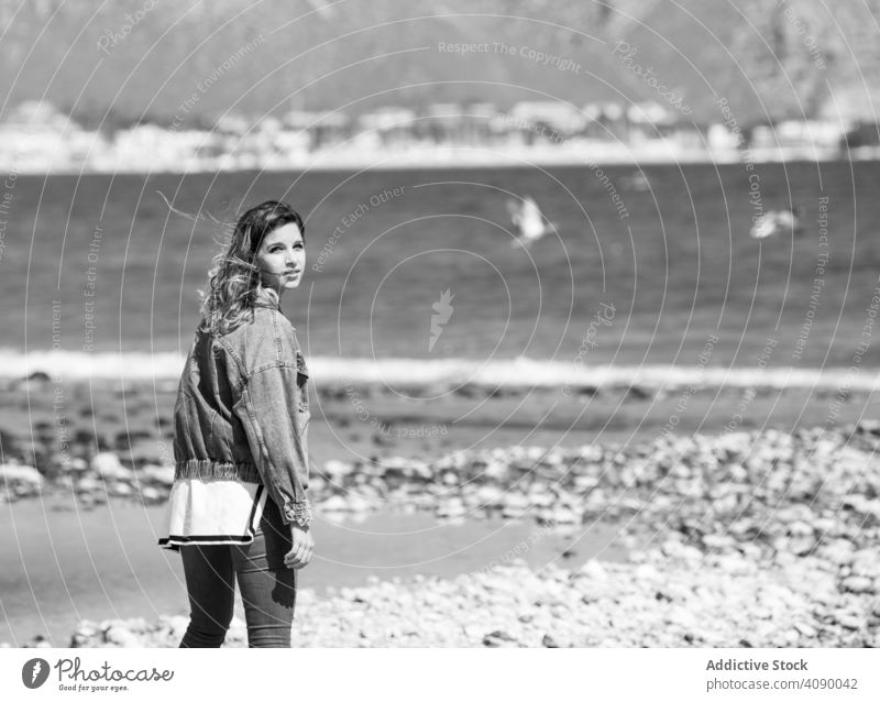 Young woman walking on seashore windy young leisure lifestyle female casual weather coast water beach rest relax sunny daytime stylish trendy denim lady dreamy